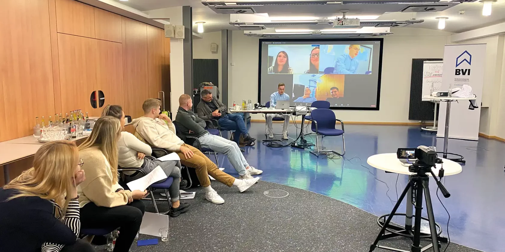 Konferenzsaal mit Anwesenden vor Ort sowie online dazugeschaltet